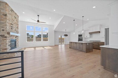 Kitchen with open floor plan, white cabinetry, light wood-style flooring, pendant lighting, and a stone fireplace