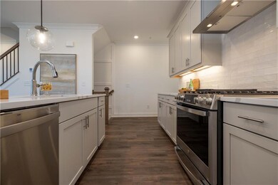 Kitchen featuring appliances with stainless steel finishes, wall chimney exhaust hood, decorative backsplash, dark wood-style flooring, and hanging light fixtures