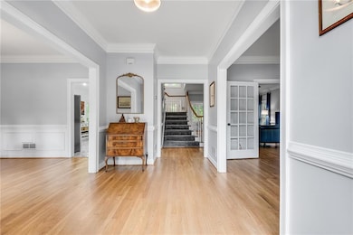 Foyer entrance featuring stairway, light wood-style floors, crown molding, and french doors