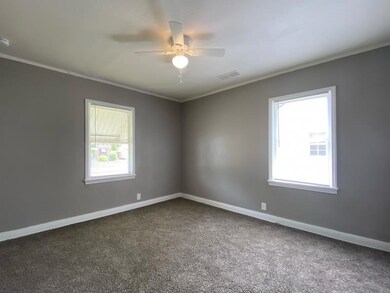Spare room featuring ornamental molding, dark colored carpet, a ceiling fan, baseboards, and a smoke detector