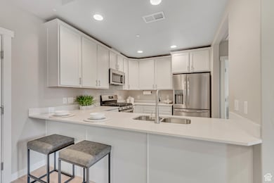 Kitchen with appliances with stainless steel finishes, recessed lighting, white cabinets, a kitchen breakfast bar, and light stone countertops