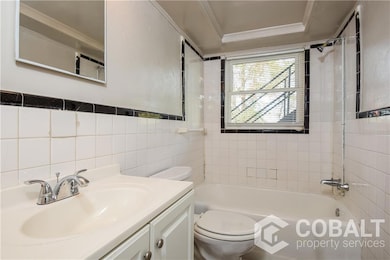 Full bathroom with ornamental molding, bathing tub / shower combination, vanity, and tile walls