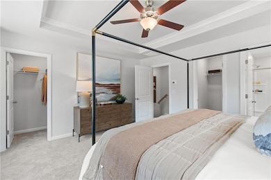 Carpeted bedroom with a walk in closet, ceiling fan, and a raised ceiling