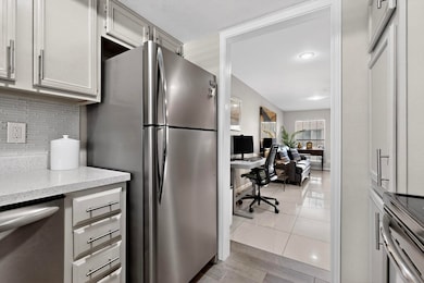 Kitchen featuring appliances with stainless steel finishes, a desk, light tile patterned flooring, tasteful backsplash, and light stone counters