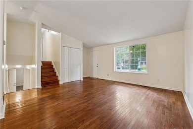 Unfurnished living room featuring hardwood / wood-style flooring, stairs, and lofted ceiling