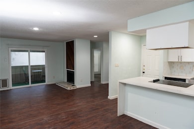 Kitchen featuring light stone counters, dark wood-style floors, backsplash, white cabinets, and a textured ceiling