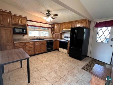 Kitchen with black appliances, under cabinet range hood, a sink, vaulted ceiling, and brown cabinetry