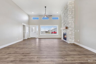Unfurnished living room featuring a ceiling fan, a stone fireplace, wood finished floors, recessed lighting, and a high ceiling