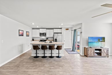 Kitchen with appliances with stainless steel finishes, light wood-style floors, white cabinets, a kitchen island with sink, and a breakfast bar area