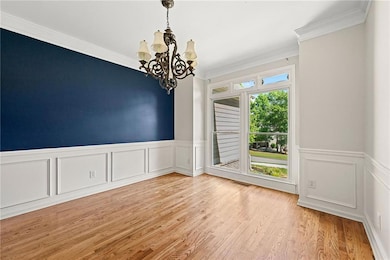 Spare room featuring a chandelier, light wood-type flooring, wainscoting, ornamental molding, and a decorative wall