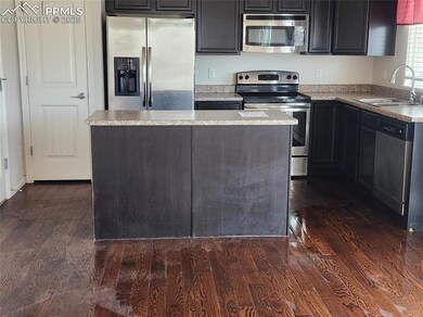Kitchen with appliances with stainless steel finishes, a sink, dark wood-style floors, a center island, and light countertops