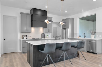 Kitchen with gray cabinetry, a breakfast bar, light wood-type flooring, tasteful backsplash, and a center island