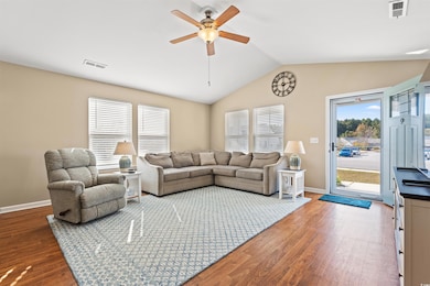 Living room featuring vaulted ceiling, healthy amount of natural light, ceiling fan, and dark wood-style floors