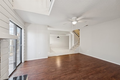 Unfurnished living room with dark wood-style flooring, ceiling fan, stairway, and a textured ceiling