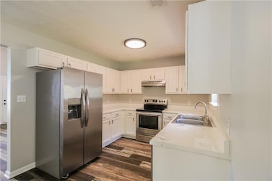 Kitchen featuring a sink, white cabinetry, appliances with stainless steel finishes, under cabinet range hood, and dark wood-style floors