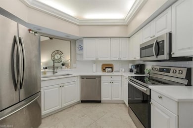 Kitchen with appliances with stainless steel finishes, white cabinetry, light countertops, light tile patterned floors, and ornamental molding