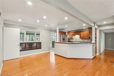 Kitchen featuring recessed lighting, brown cabinets, light wood-type flooring, stainless steel appliances, and dark stone countertops