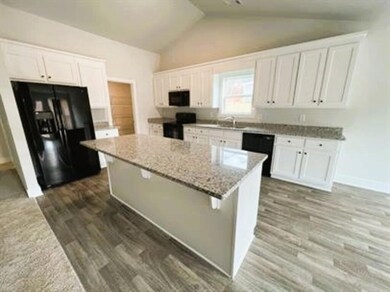 Kitchen featuring white cabinets, black appliances, dark wood-style flooring, vaulted ceiling, and light stone counters