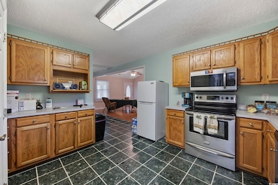 Kitchen with appliances with stainless steel finishes, light countertops, dark tile patterned floors, a textured ceiling, and brown cabinetry