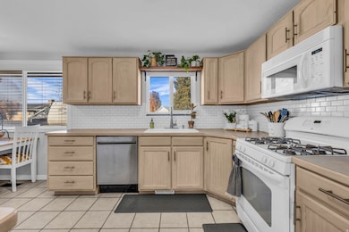 Kitchen featuring light brown cabinetry, white appliances, and tasteful backsplash