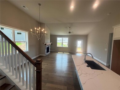 Unfurnished living room with vaulted ceiling, dark wood-type flooring, a chandelier, a stone fireplace, and stairway
