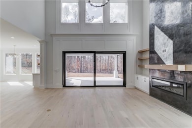 Unfurnished living room featuring a glass covered fireplace, a chandelier, light wood finished floors, recessed lighting, and a high ceiling