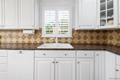 Kitchen with white dishwasher, stone countertops, backsplash, and white cabinetry