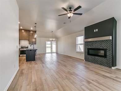Unfurnished living room featuring a tiled fireplace, vaulted ceiling, light wood-style flooring, a chandelier, and ceiling fan