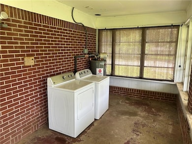 Laundry room featuring brick wall, electric water heater, and washing machine and clothes dryer