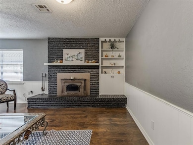 Living room featuring wainscoting, a textured ceiling, dark wood-style flooring, and a brick fireplace