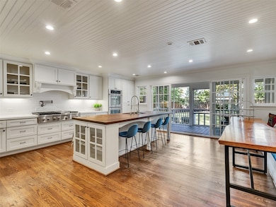 This spacious kitchen features a large island with seating, modern gourmet appliances, and ample cabinetry. It opens to a bright area with large windows and doors leading to a screened in porch, offering a seamless indoor-outdoor flow. Perfect for entertaining and family gatherings.