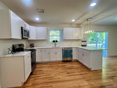 Kitchen with stainless steel appliances, a peninsula, white cabinetry, and recessed lighting
