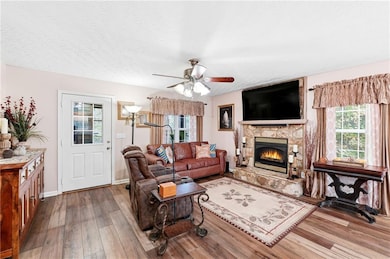 Living area featuring ceiling fan, healthy amount of natural light, a stone fireplace, wood-type flooring, and a textured ceiling
