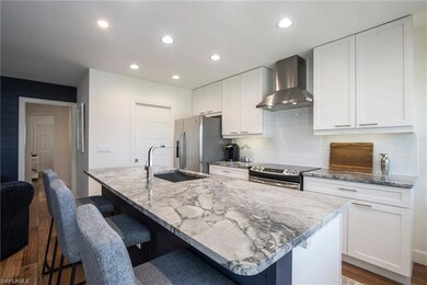 Kitchen featuring a center island with sink, white cabinets, appliances with stainless steel finishes, wall chimney range hood, and a sink