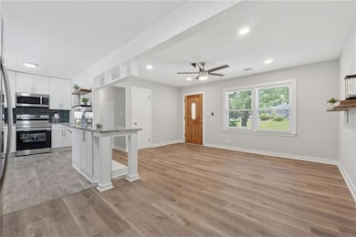 Kitchen with stainless steel appliances, open shelves, white cabinets, a breakfast bar area, and a ceiling fan