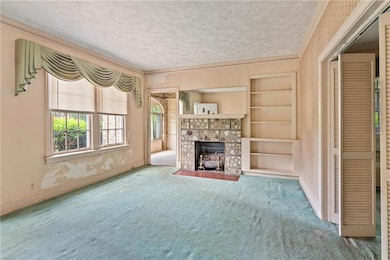 Unfurnished living room featuring carpet, a fireplace with flush hearth, baseboards, a textured ceiling, and crown molding