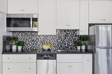 This stylish kitchen combines contemporary design with everyday functionality. Featuring crisp white cabinetry, elegant black stone countertops, and a striking mosaic tile backsplash, the space exudes modern sophistication. The high-end induction cooktop offers precise temperature control and energy efficiency, complemented by stainless-steel appliances and a deep chrome sink. Beautifully updated culinary space — perfect for both cooking and entertaining.