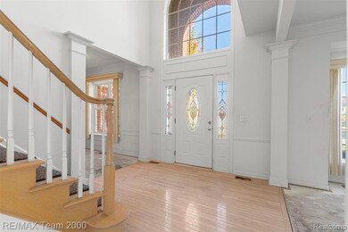 Entrance foyer featuring decorative columns, stairs, light wood-style floors, and a high ceiling