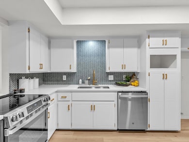 Kitchen featuring stainless steel appliances, tasteful backsplash, white cabinets, and light wood-type flooring