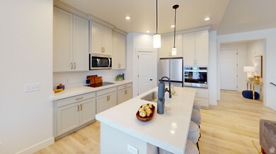 Kitchen with stainless steel appliances, light wood-style flooring, a kitchen island with sink, a sink, and hanging light fixtures