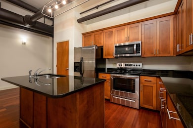 Kitchen featuring stainless steel appliances, dark wood finished floors, brown cabinetry, and dark stone countertops