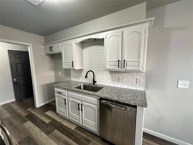 Kitchen with stainless steel dishwasher, a sink, baseboards, and light stone countertops