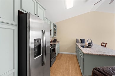 Kitchen with stainless steel appliances, a sink, a peninsula, light wood finished floors, and lofted ceiling