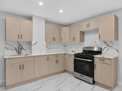 Kitchen with light brown cabinetry, stainless steel gas range, light marble finish floors, light stone counters, and recessed lighting