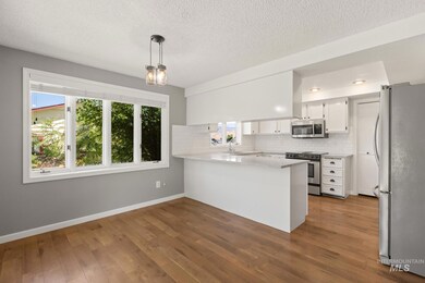 Kitchen featuring a peninsula, stainless steel appliances, backsplash, wood finished floors, and white cabinets