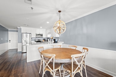 Dining room with a wainscoted wall, a chandelier, dark wood finished floors, crown molding, and recessed lighting