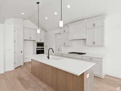 Kitchen with oven, stainless steel microwave, custom range hood, lofted ceiling, and light wood finished floors