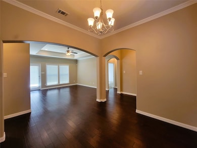 Unfurnished room featuring arched walkways, ornamental molding, dark wood finished floors, a chandelier, and a tray ceiling
