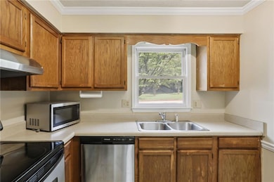 Kitchen featuring appliances with stainless steel finishes, brown cabinets, crown molding, and light countertops