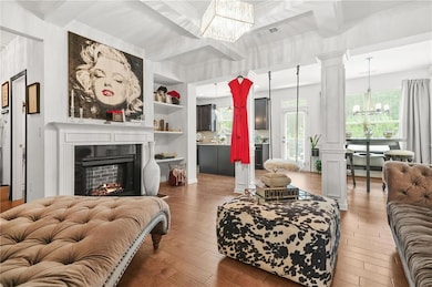 Living area featuring a chandelier, ornamental molding, wood-type flooring, beam ceiling, and a warm lit fireplace